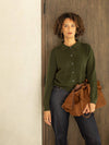 Woman wearing a green sweater and holding a brown leather bag against a wooden door.