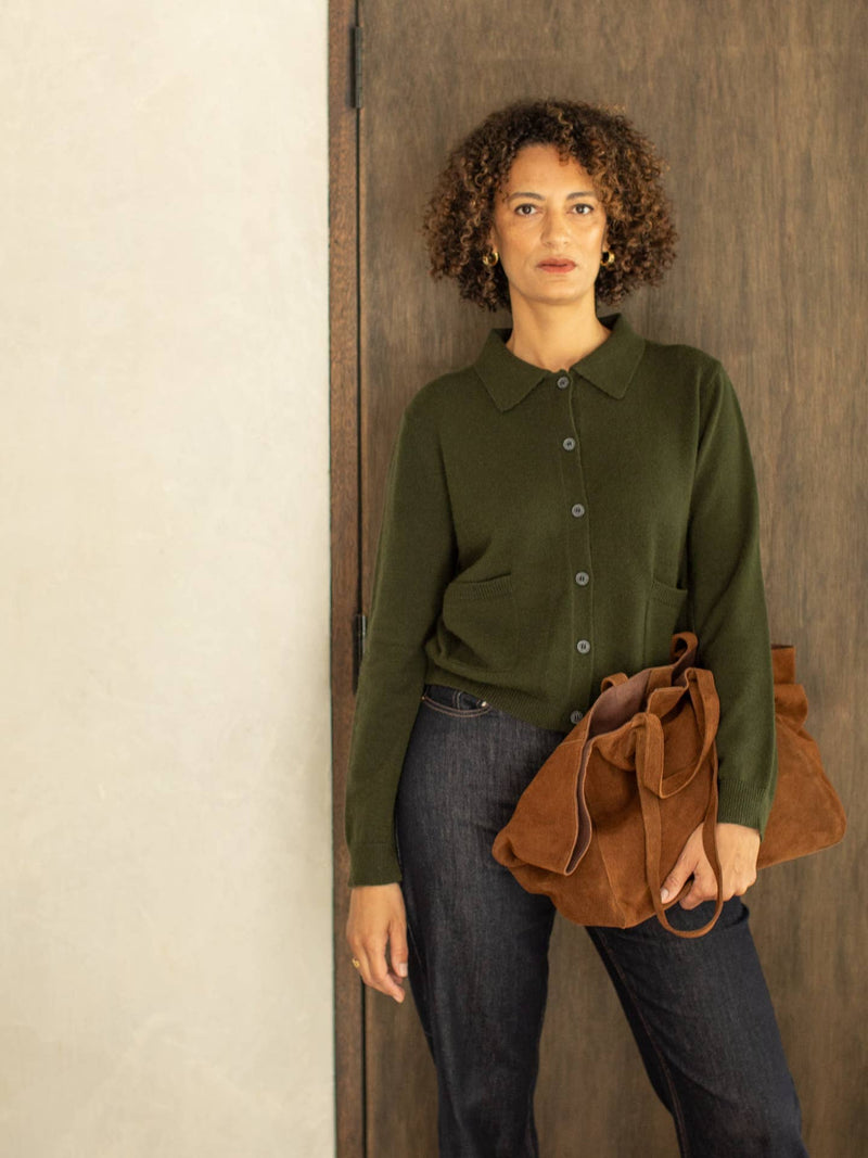 Woman wearing a green sweater and holding a brown leather bag against a wooden door.