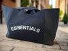 Black tote bag with 'ESSENTIALS' text on a light background
