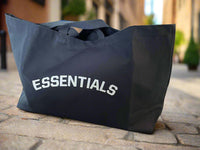 Black tote bag with 'ESSENTIALS' text on a light background