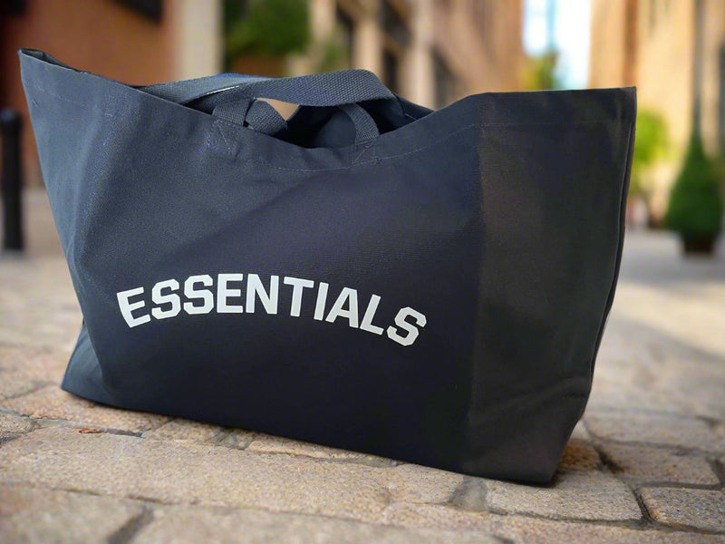 Black tote bag with 'ESSENTIALS' text on a light background