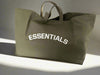 Green tote bag with 'ESSENTIALS' text on a light gray background