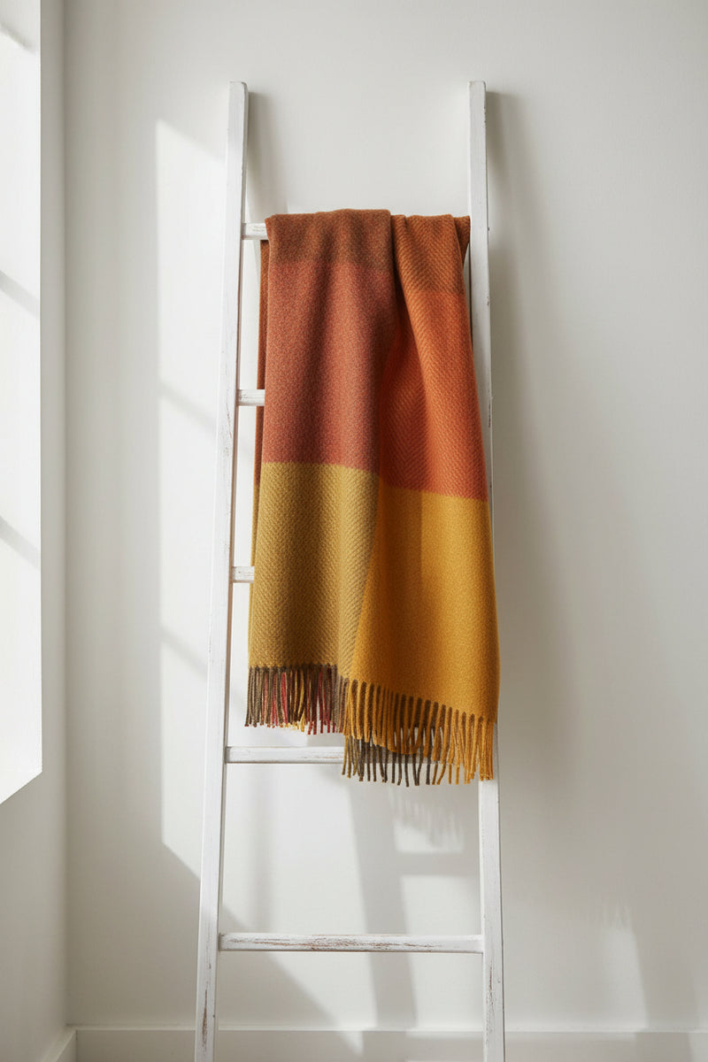 A rectangular woven throw with a checkered pattern in warm autumn colors, featuring a herringbone weave and fringed edges on a white background.