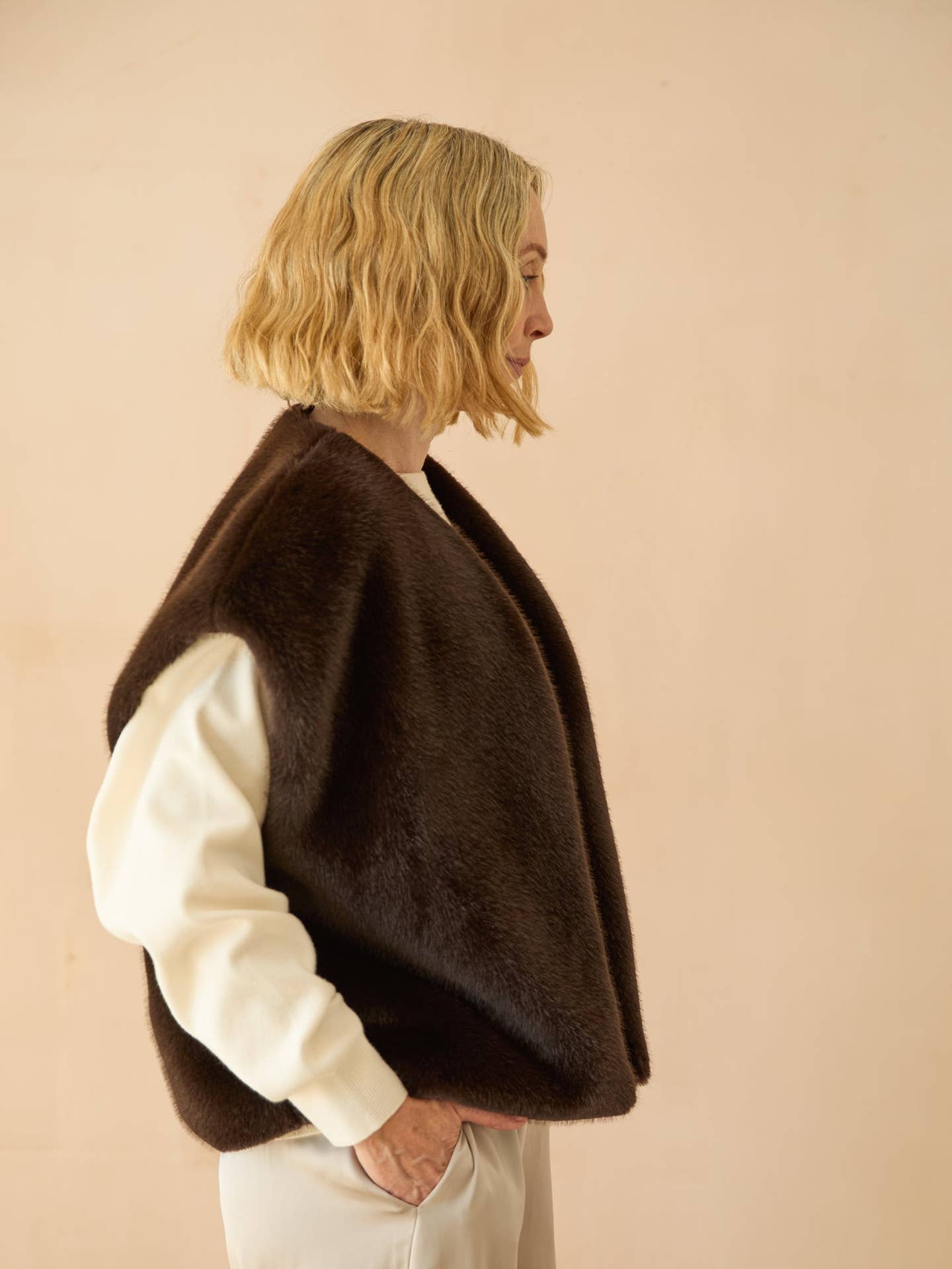Person wearing a brown poncho over a white shirt against a beige background
