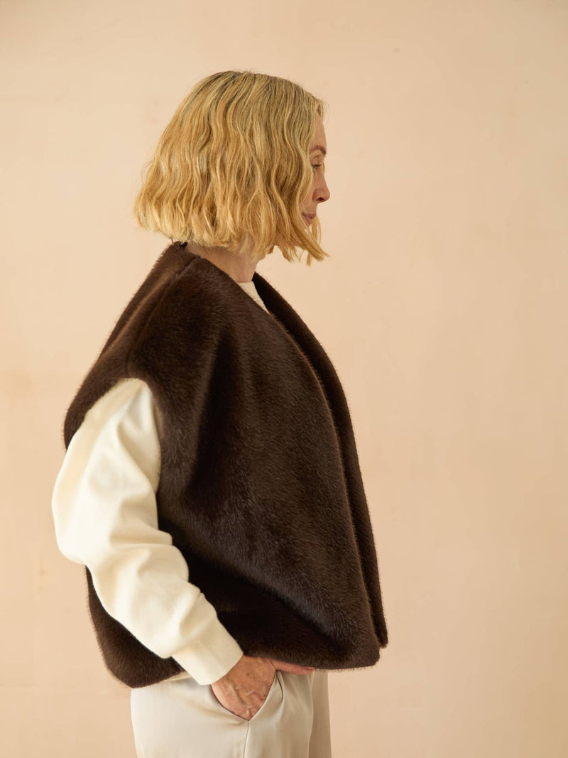 Person wearing a brown poncho over a white shirt against a beige background