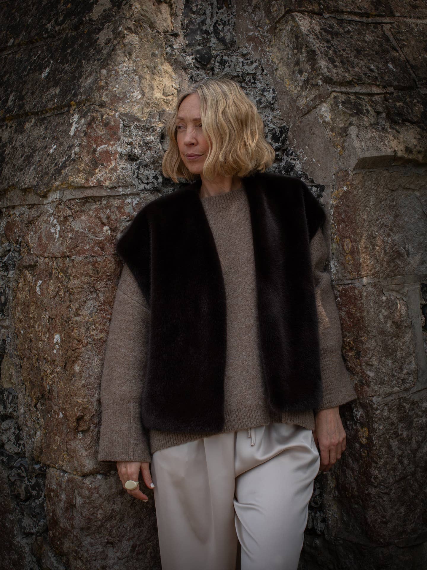 Person wearing a black vest over a gray sweater against a stone wall
