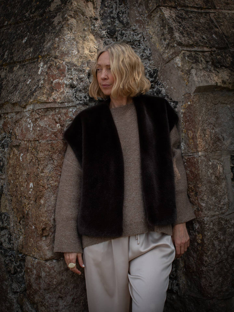 Person wearing a black vest over a gray sweater against a stone wall