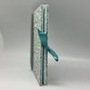 Two books bound together with a teal ribbon on a gray background