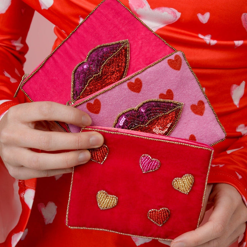 Person holding a red and pink clutch with heart designs against a red background with white hearts.
