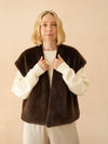 Woman wearing a brown vest over a white shirt against a beige background