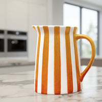 Ceramic pitcher with orange and white vertical stripes on a white background