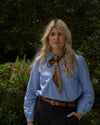 Woman wearing a blue shirt with a brown scarf and black pants outdoors.