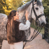Woman petting a gray horse on a path with trees in the background