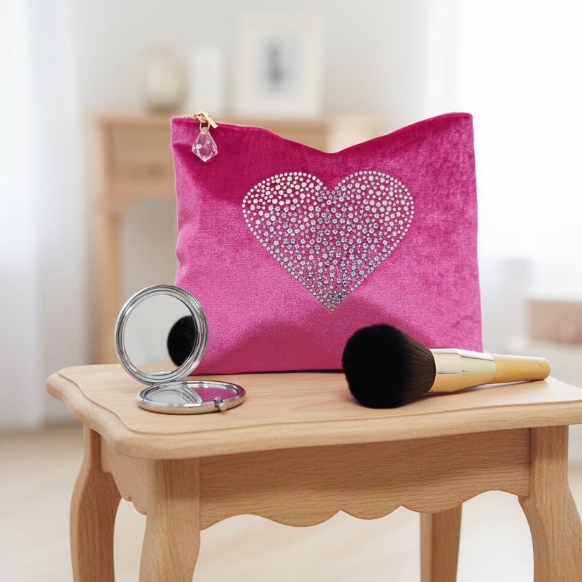 Pink pouch with heart design, makeup brush, and compact mirror on a white background