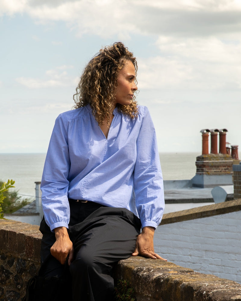 Person wearing a light blue shirt and dark pants sitting on a ledge with a scenic background.