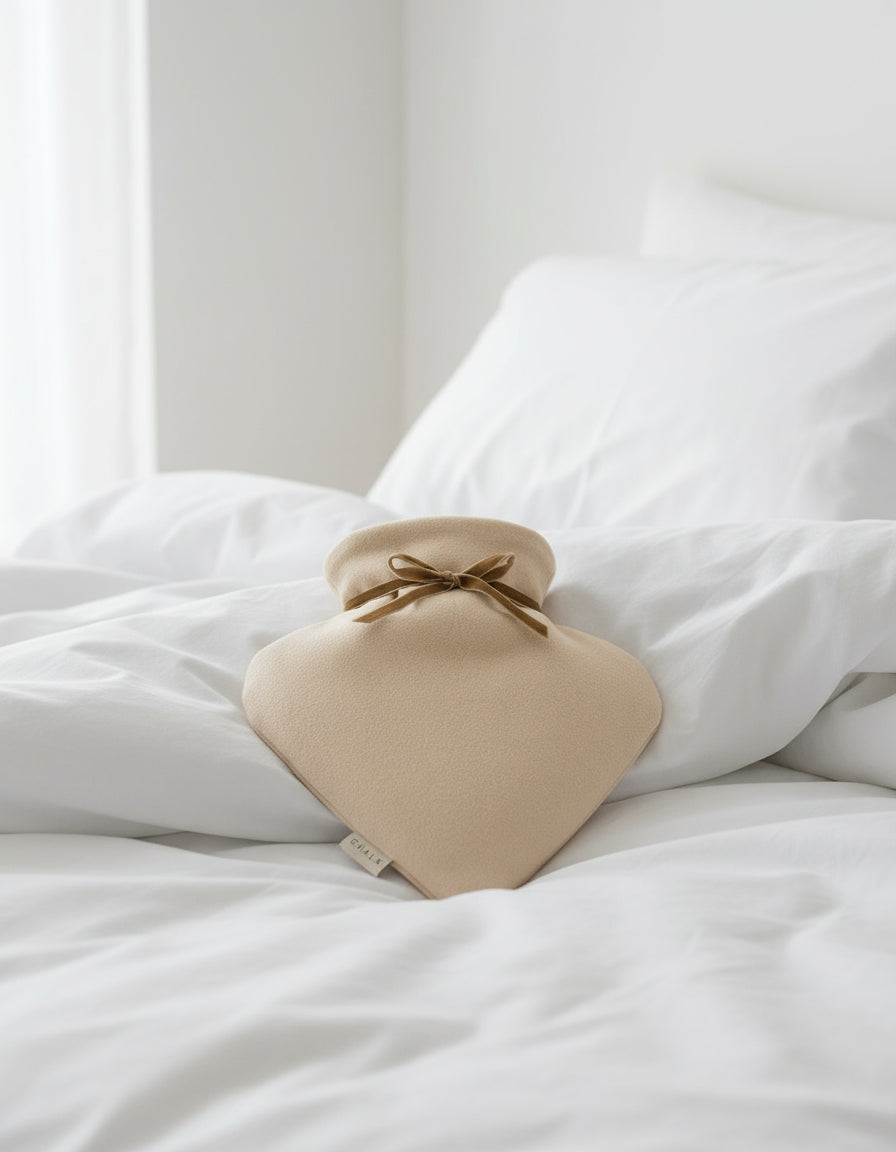 Beige hot water bottle with a brown ribbon on a white background