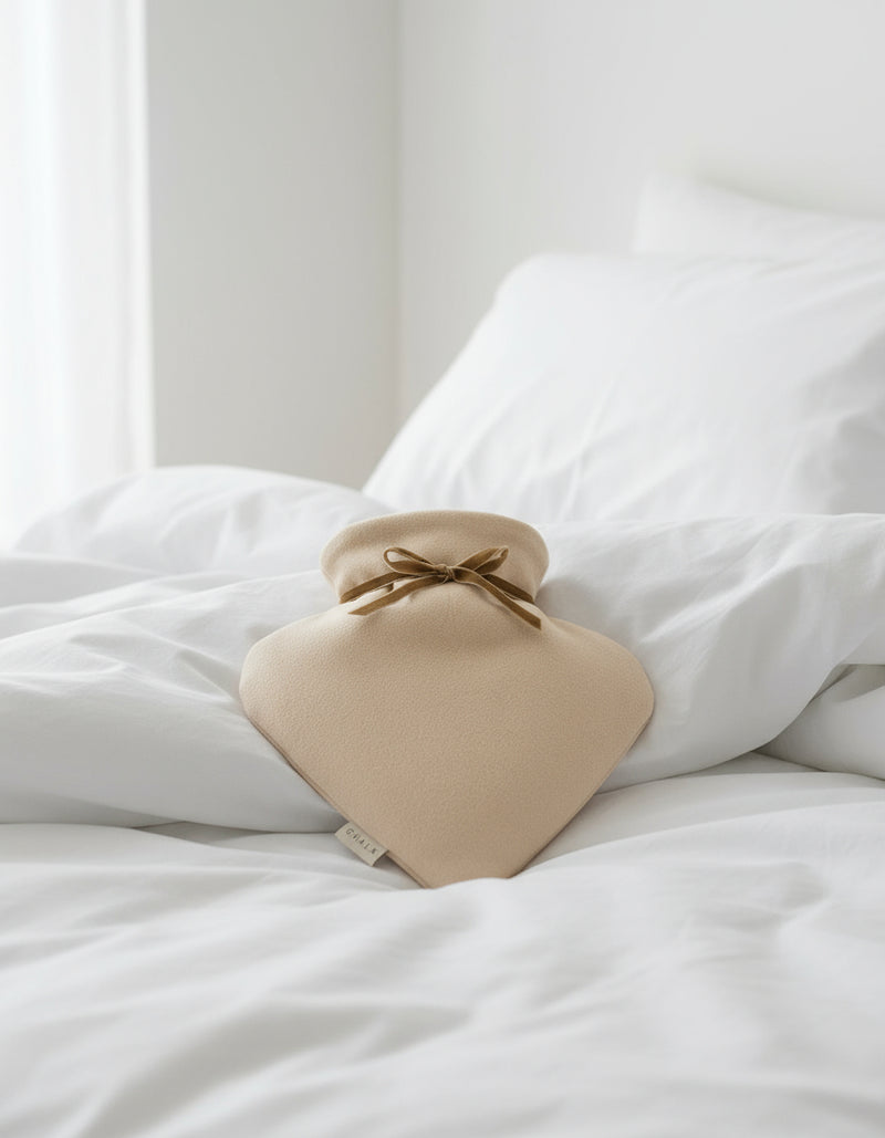 Beige hot water bottle with a brown ribbon on a white background
