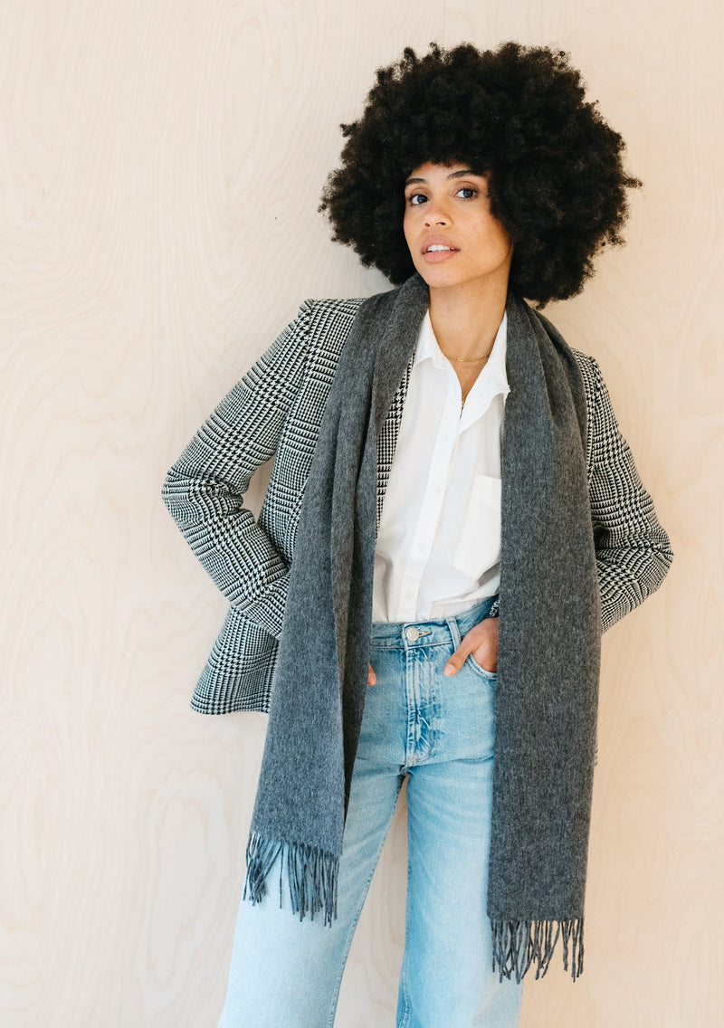 Woman wearing a plaid jacket, white shirt, and light blue jeans with a gray scarf against a beige background