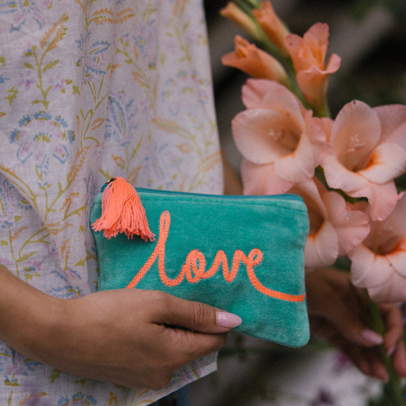 Person holding a turquoise pouch with 'love' in orange, surrounded by pink flowers.