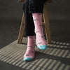 Person wearing pink socks with black patterns and blue toes, sitting on a wooden stool.