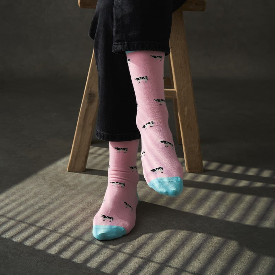 Person wearing pink socks with black patterns and blue toes, sitting on a wooden stool.