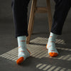 Person wearing light blue socks with orange tips and fox patterns, standing on a dark floor.