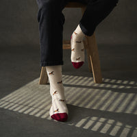 Person wearing socks with horse pattern and red toes, sitting on a wooden stool.