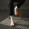 Person wearing white socks with orange tips and patterns, sitting on a wooden stool.