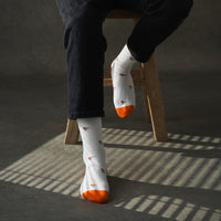 Person wearing white socks with orange tips and patterns, sitting on a wooden stool.