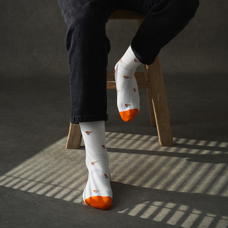 Person wearing white socks with orange tips and patterns, sitting on a wooden stool.