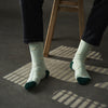Person wearing light green socks with small patterns, sitting on a wooden stool.