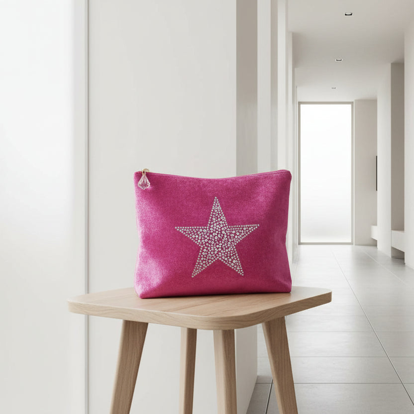 Pink clutch bag with star design and makeup items on a white background