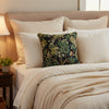 Decorative pillow with nature-themed pattern featuring leaves, flowers, and birds on a black background.