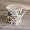 White mug with nature-themed design featuring leaves and birds on a marble surface.