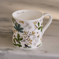 White mug with nature-themed design featuring leaves and birds on a marble surface.