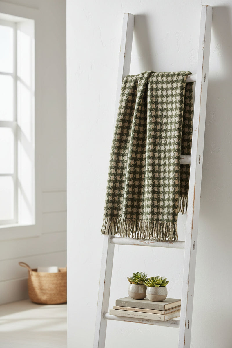 A woven throw with a houndstooth pattern in dark olive green and beige, finished with fringed edges.