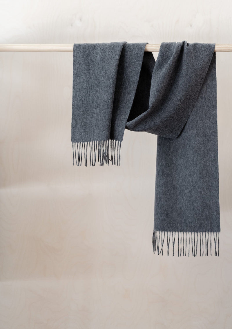 Gray scarf with fringes draped over a wooden rod against a neutral background