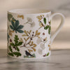 White mug with nature-themed design featuring leaves and birds on a neutral background