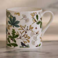 White mug with nature-themed design featuring leaves and birds on a neutral background