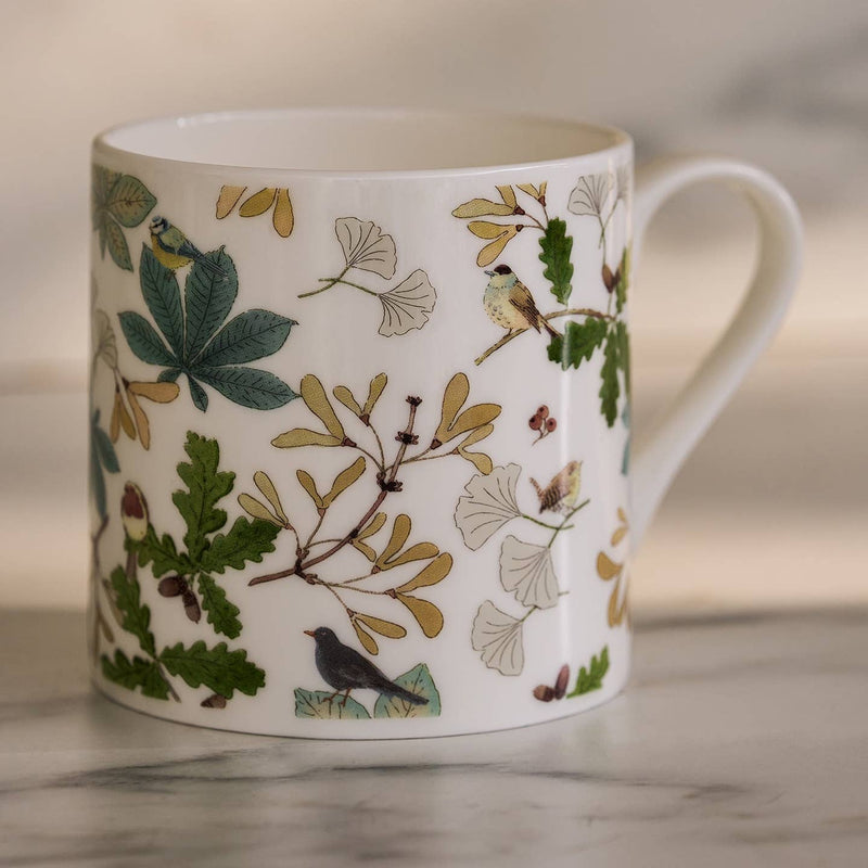 White mug with nature-themed design featuring leaves and birds on a neutral background