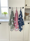 Set of three patterned sheep tea towels hanging on a rack with a kitchen background.
