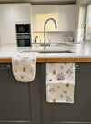 Kitchen setting with a towel and oven glove hanging on a cabinet, featuring watering can patterns.