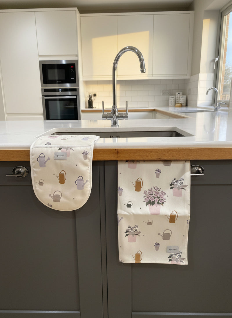 Kitchen setting with a towel and oven glove hanging on a cabinet, featuring watering can patterns.